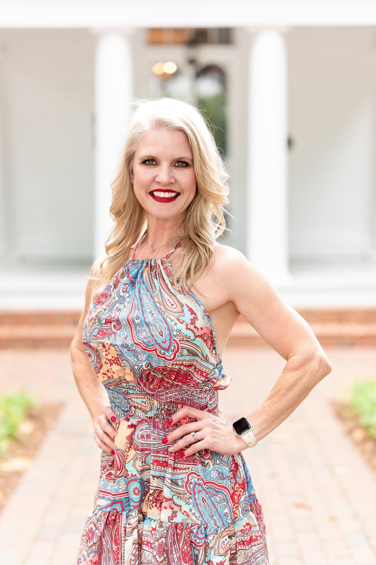 Woman in colorful paisley dress with hands on hips, smiling outdoors.