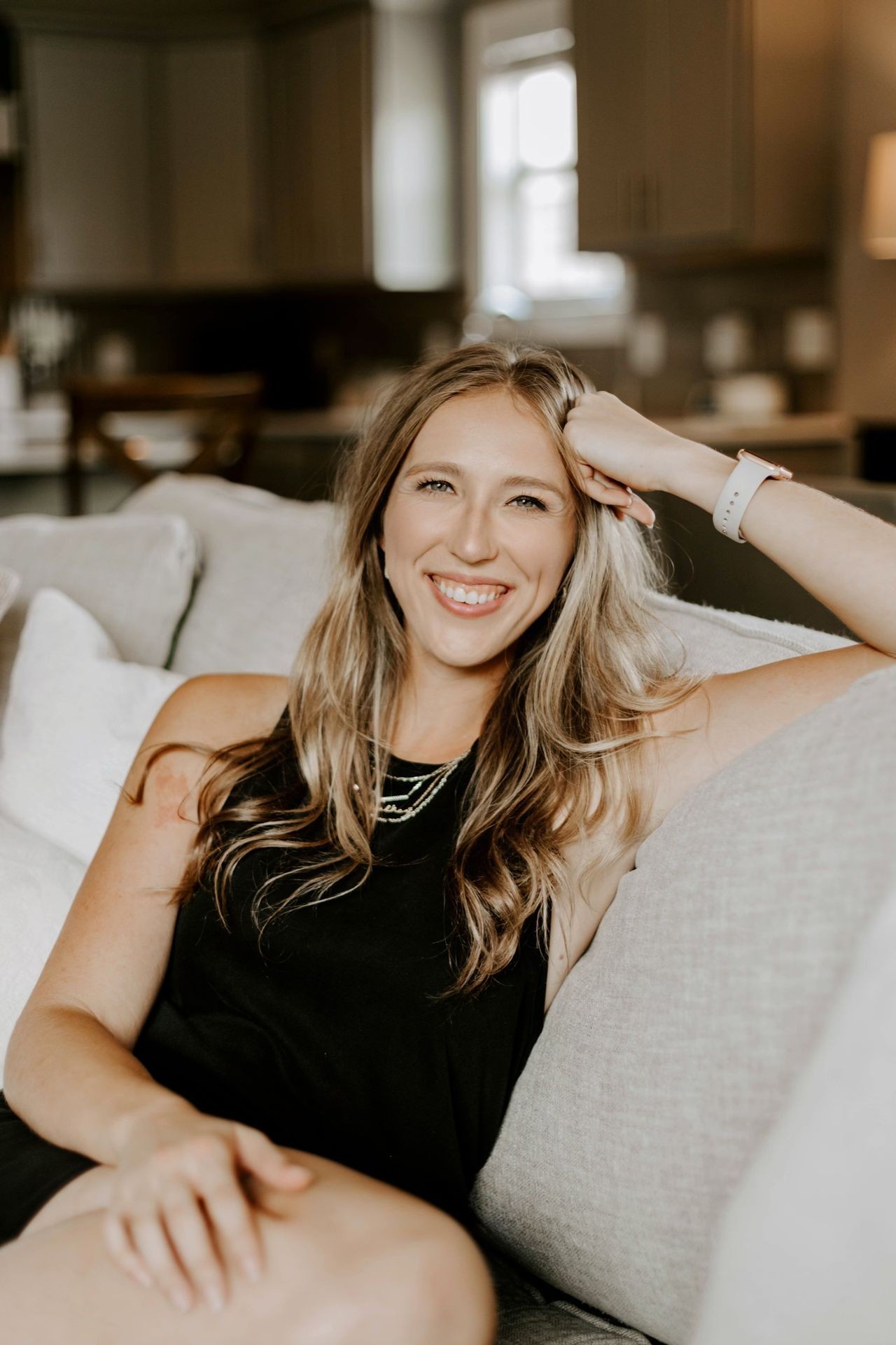 Smiling woman with long hair lounging on a couch in a cozy living room setting.